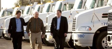 Three men walking next to a row semi-trucks parked.