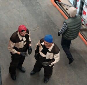 Picture of 3 men standing and walking in a cold storage warehouse wearing cold weather gear.